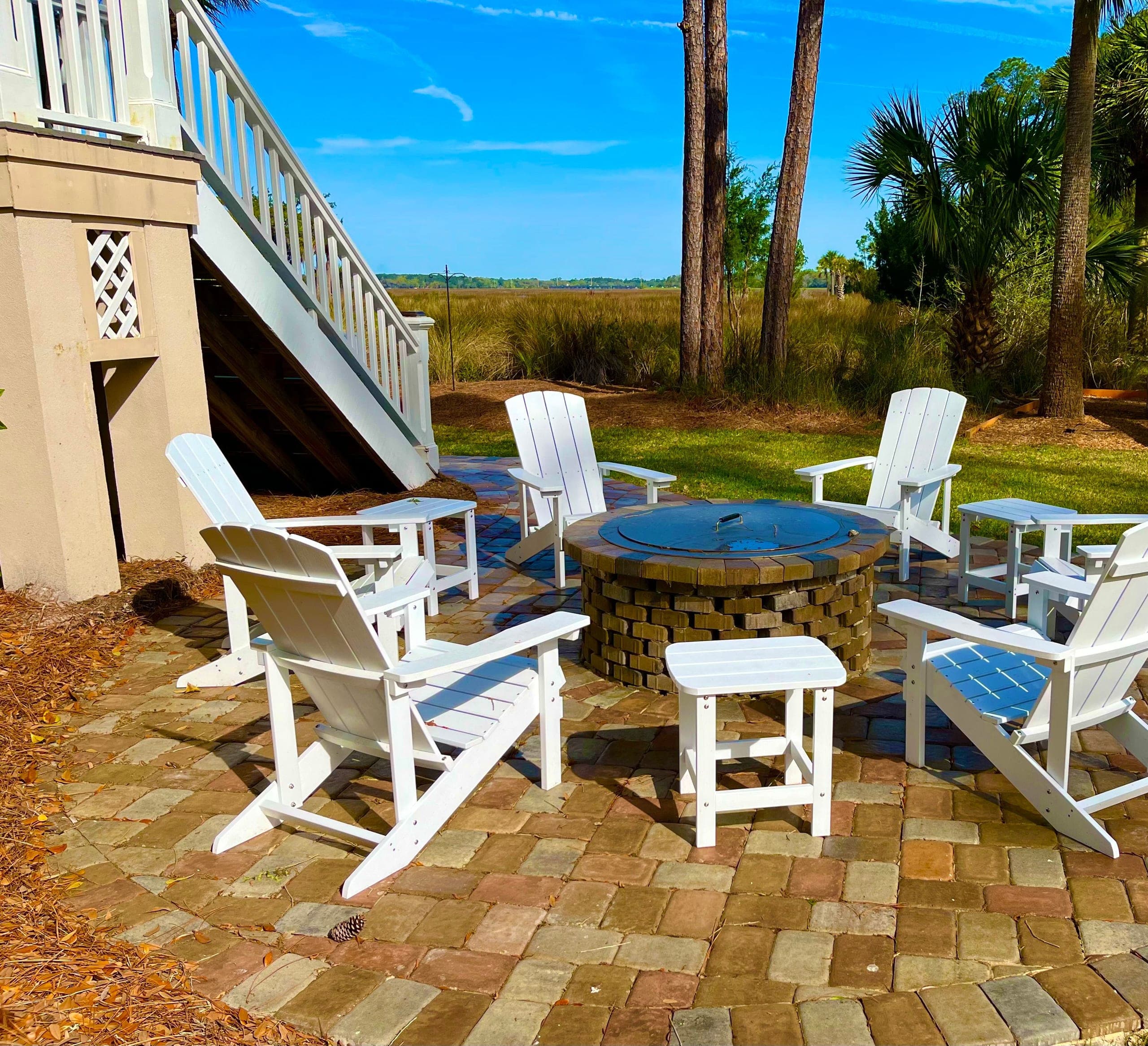 A fire-pit terrace at the lawn's edge, pines and palmettos opening to the marsh.