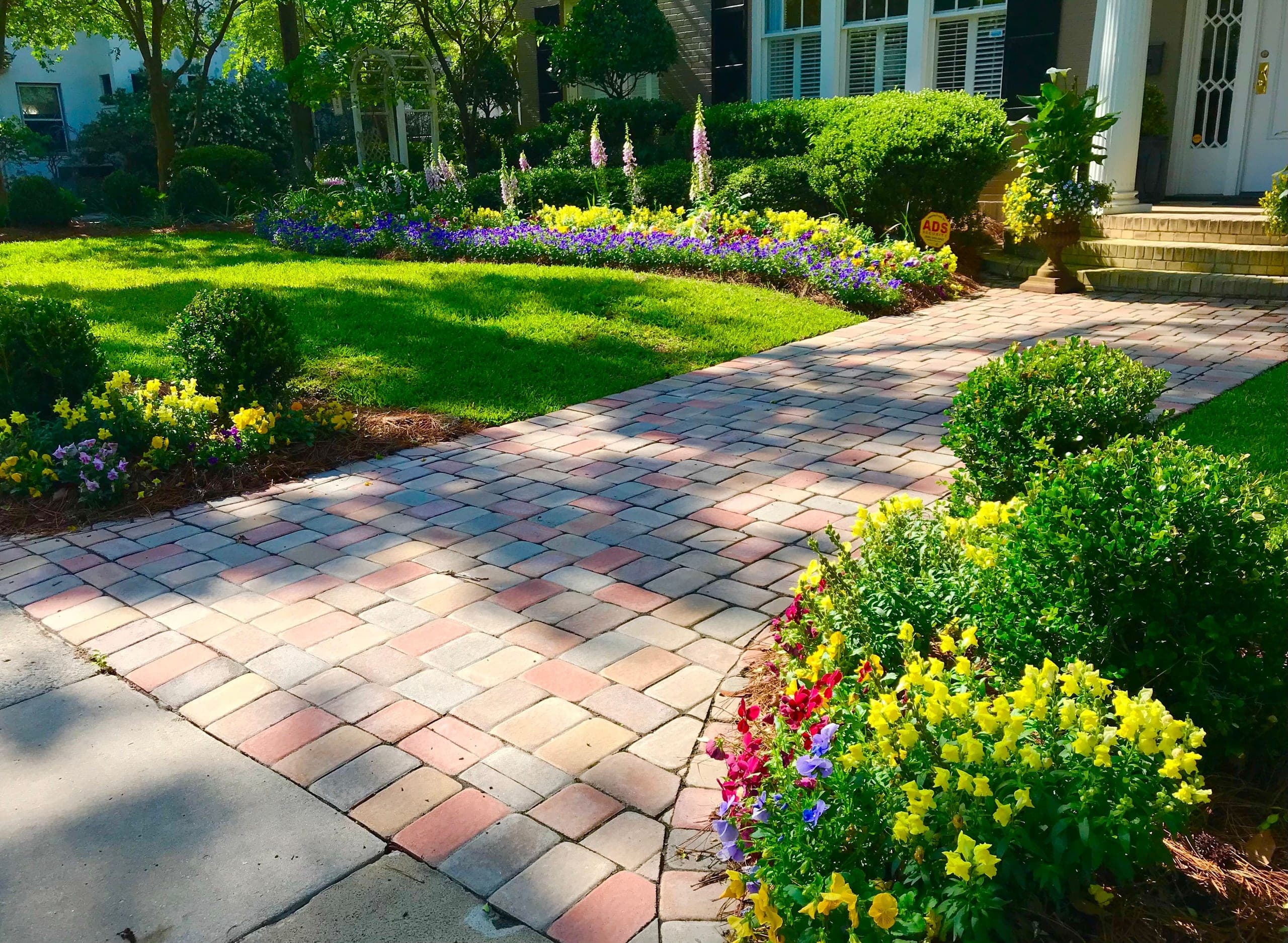 A paver walk leads through boxwood and spring borders to a columned entry.