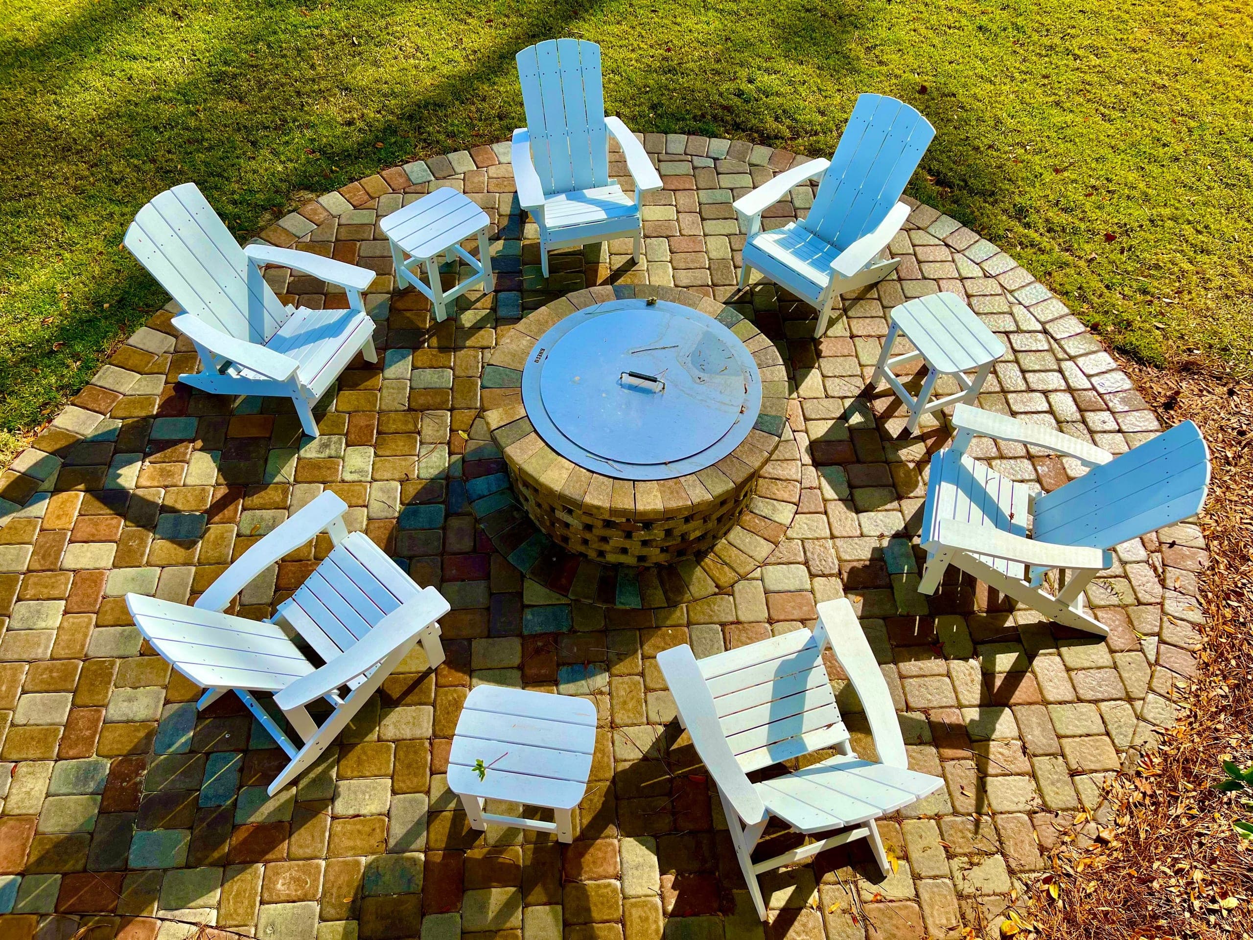Looking down on a circular paver terrace, Adirondack chairs ringing a brick fire pit.