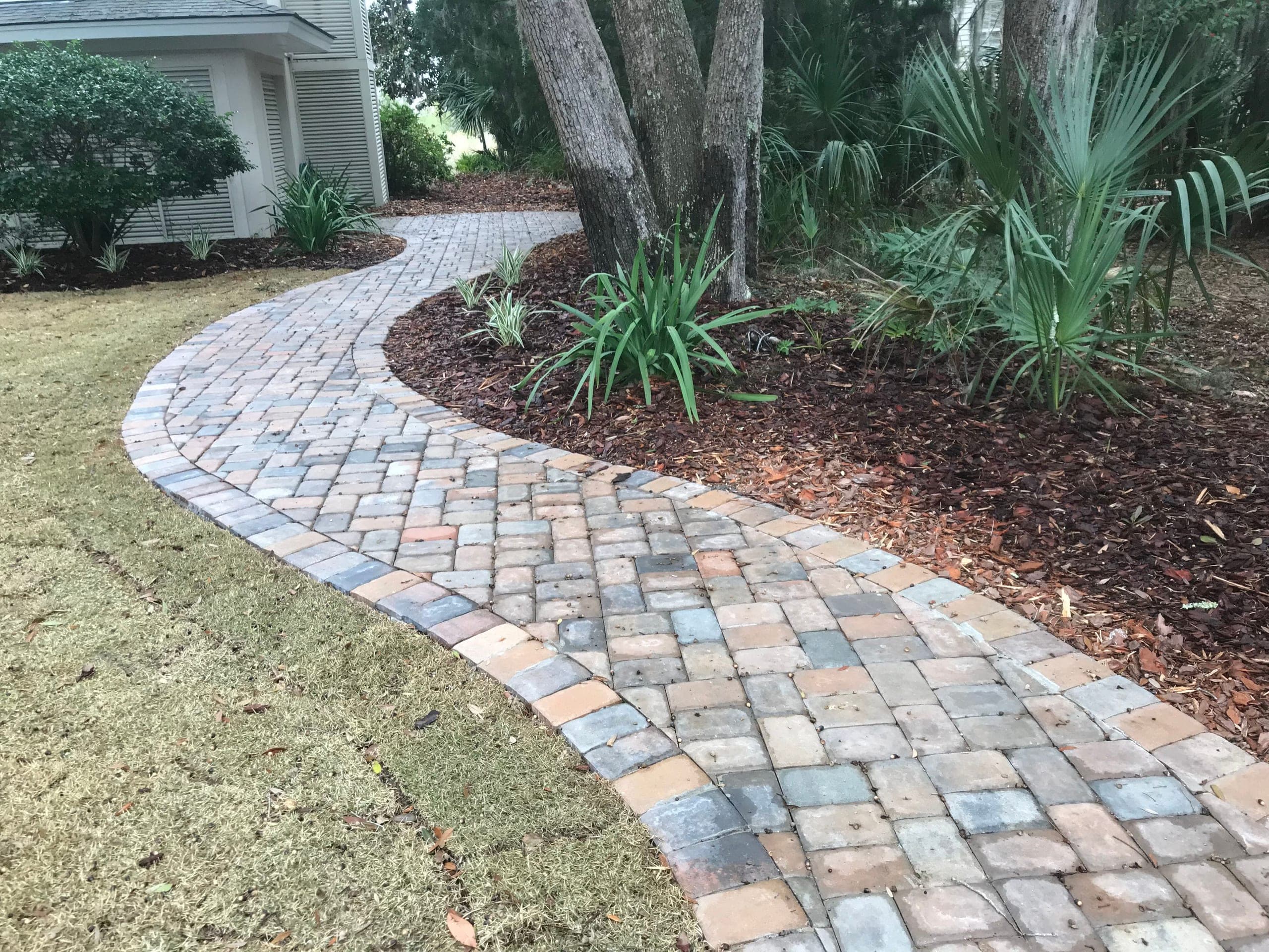 A paver walk curves between lawn and mulched beds toward the door.