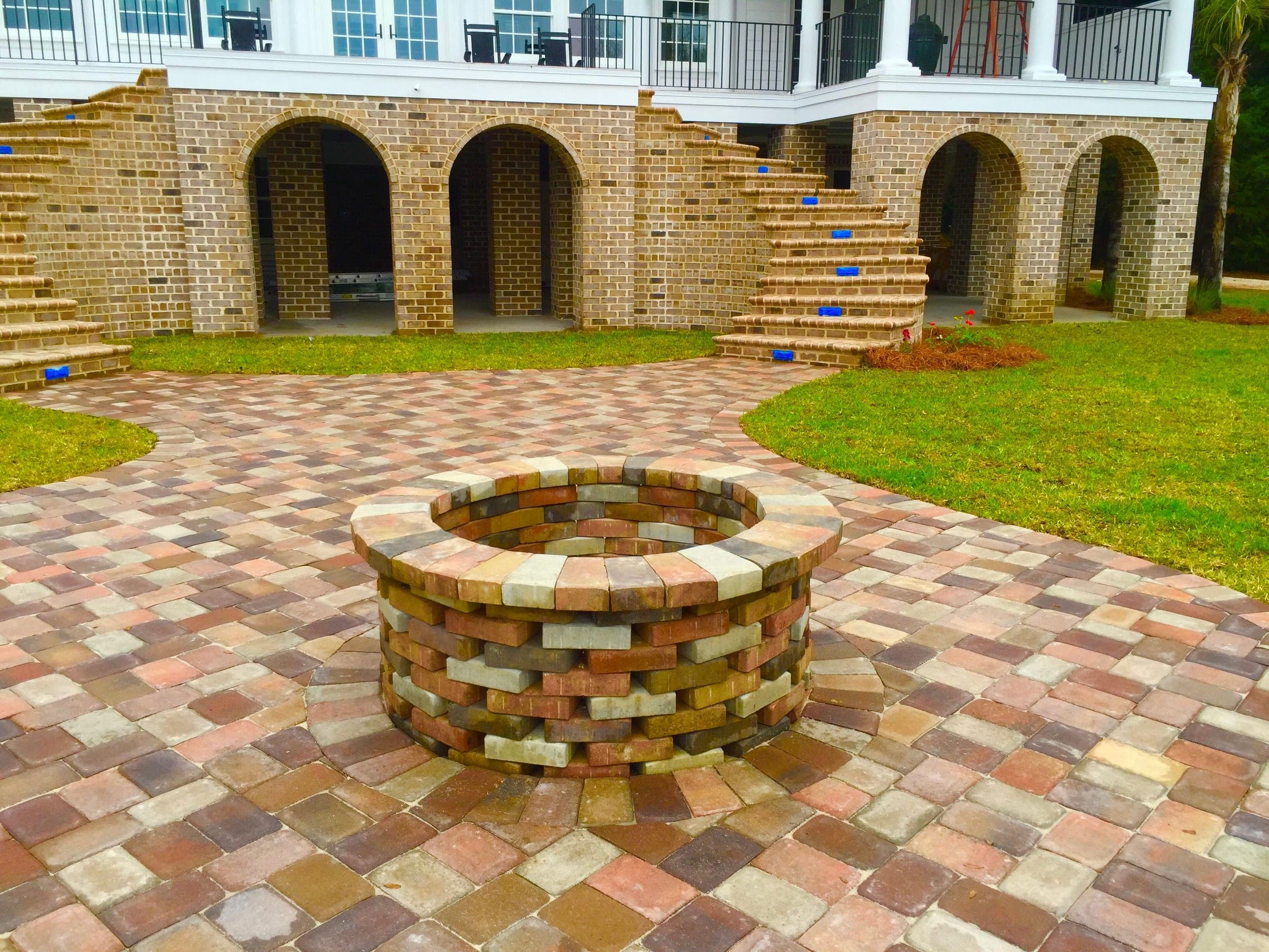 A brick fire pit and paver court complete below the new stairs, punch-list tape still on the treads.