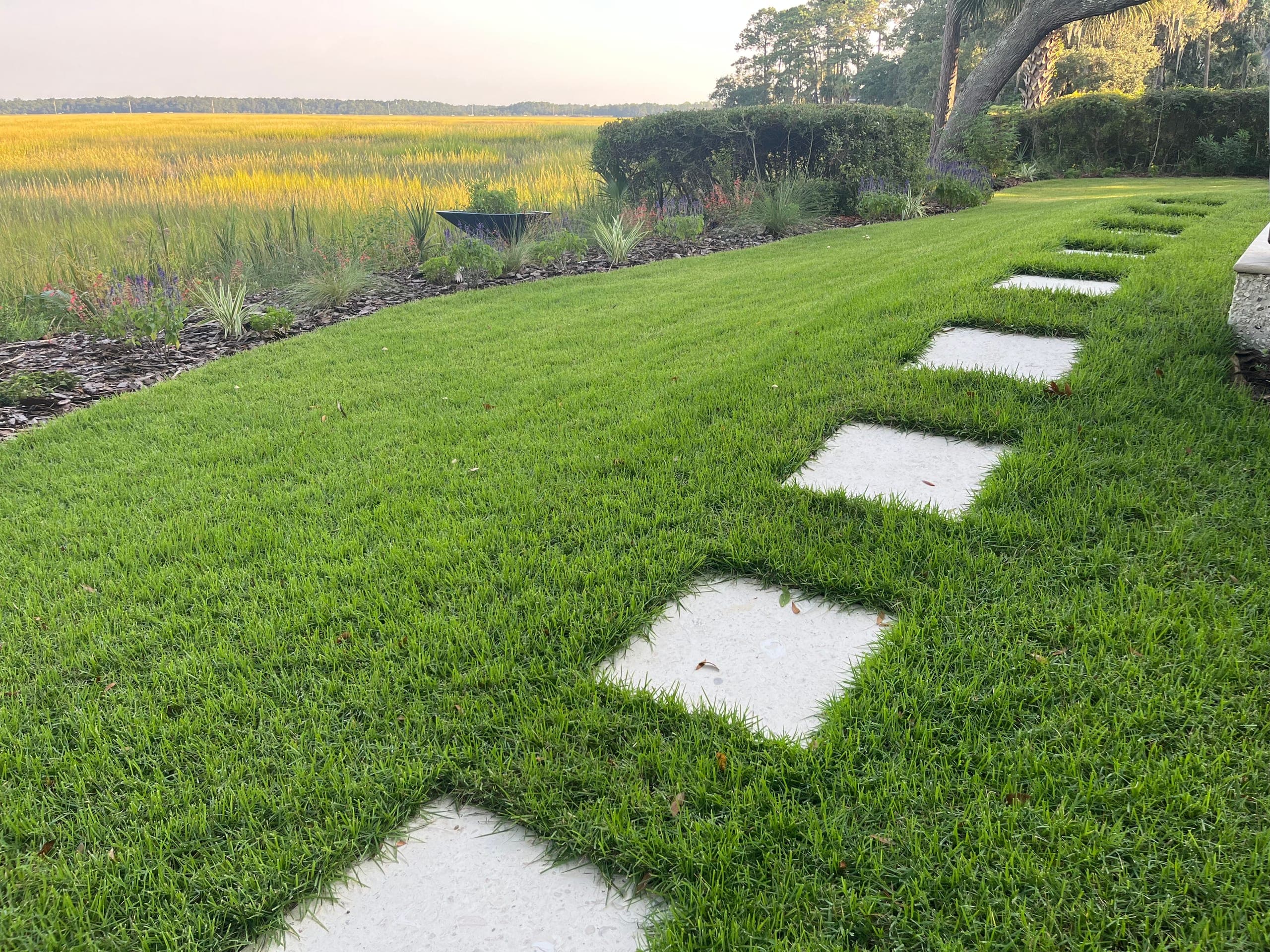 Square stone steppers set diagonally into the lawn along a marsh-front border.
