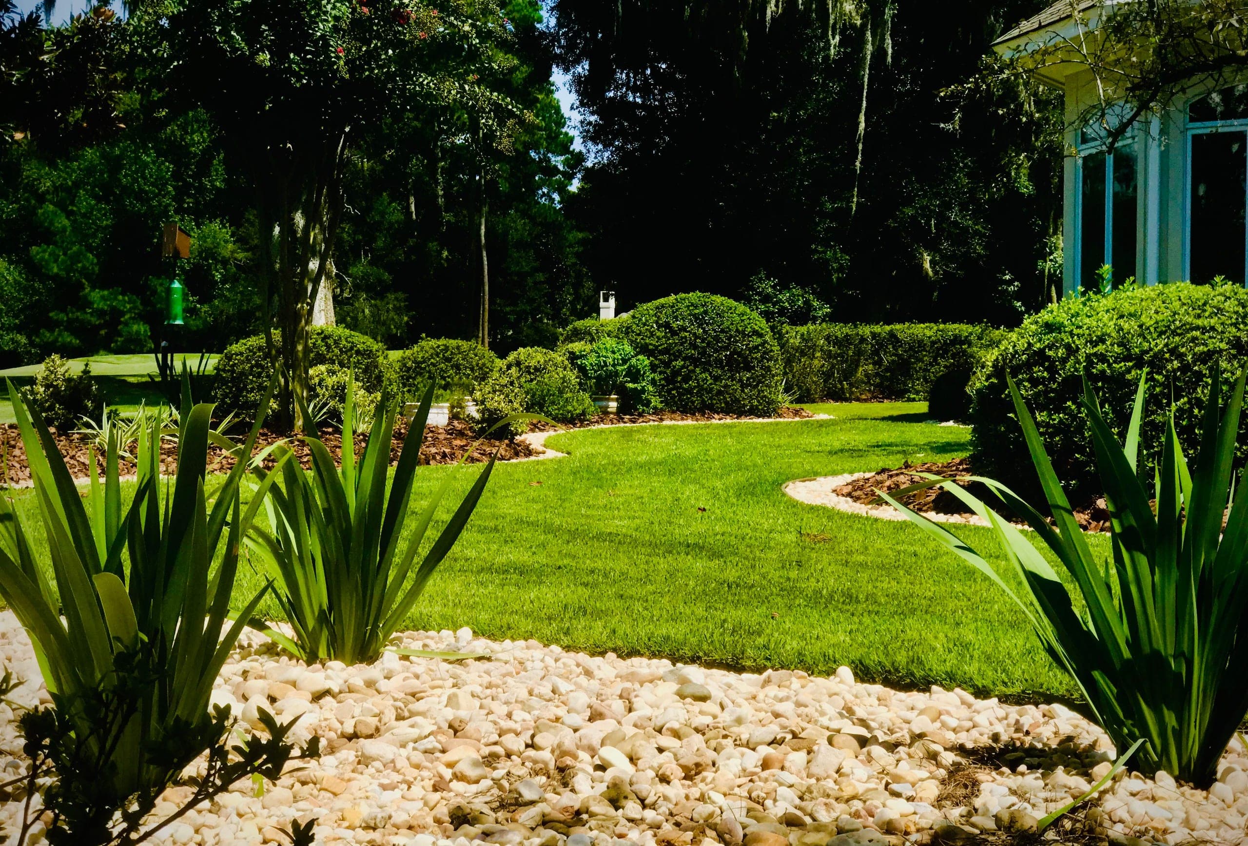 A ribbon of lawn winds between pebble-bordered beds and clipped hedges.